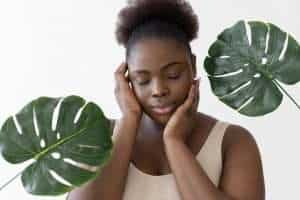 Woman with natural nails and lush green leaves, promoting nail health and beauty.