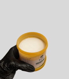 Body lotion in a yellow jar with a black-gloved hand holding it.