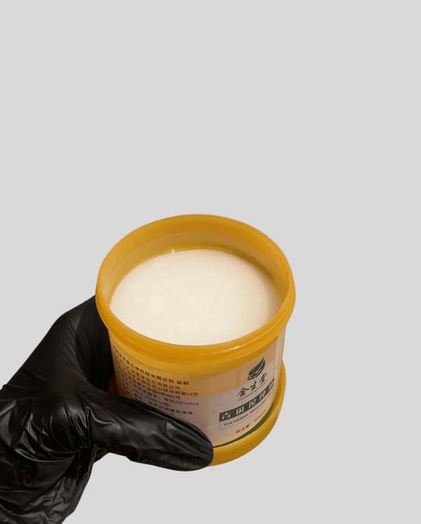 Moisturizing Body Lotion Body lotion in a yellow jar with a black-gloved hand holding it.
